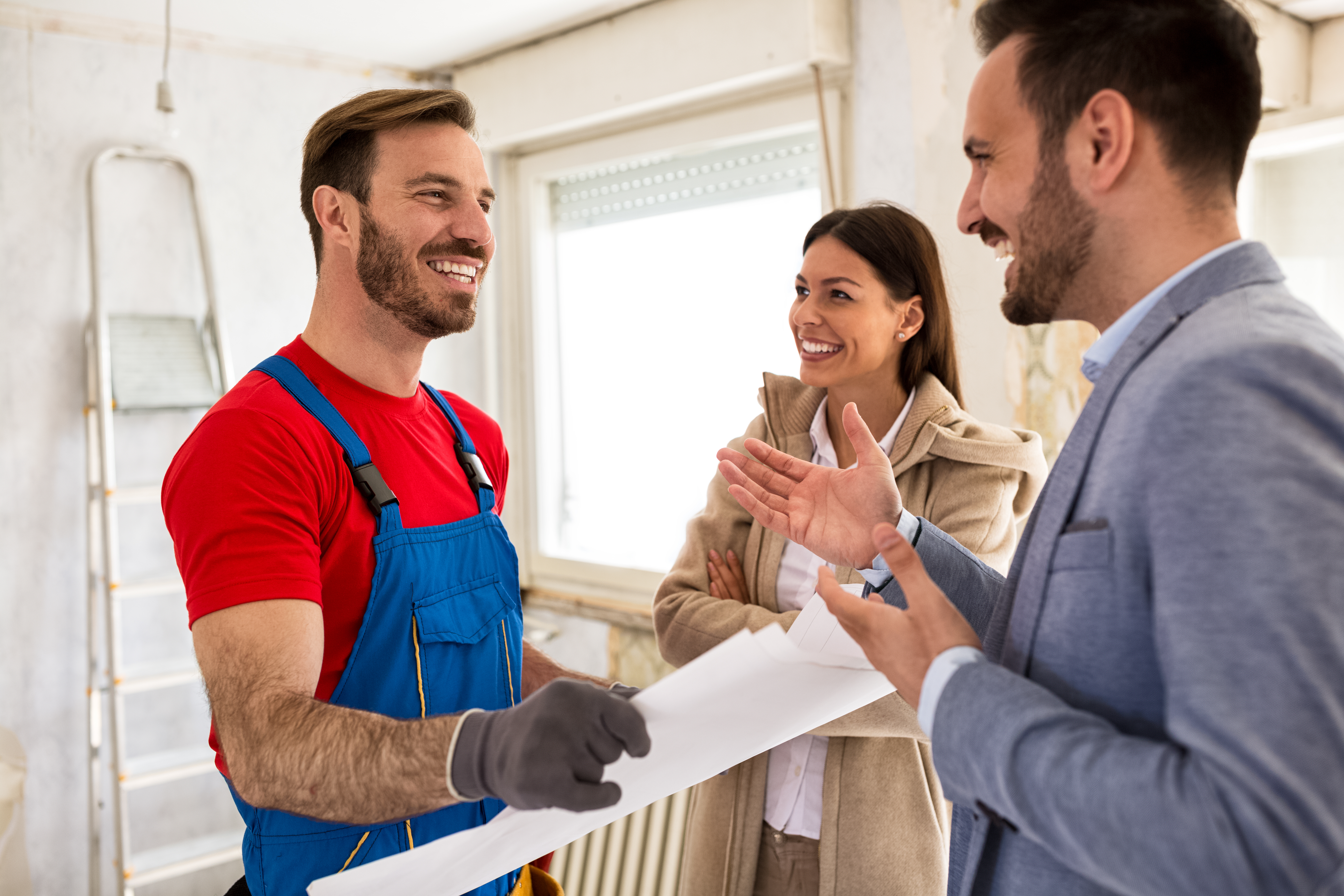 Young smiling couple and handyman talking about details of renovations home
