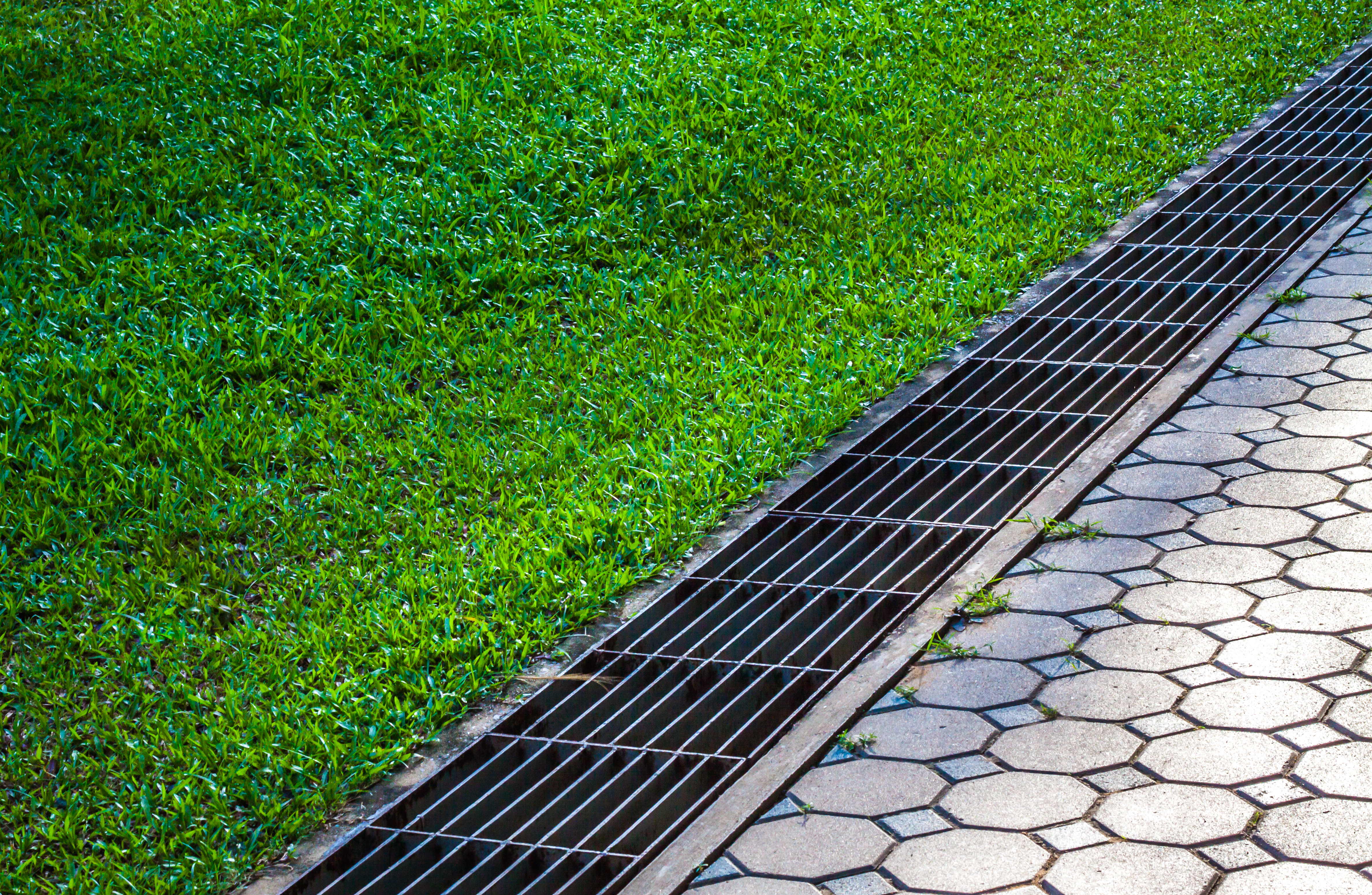waterway and road - grass. Aqueduct between nature and city. iron grate of water drain in grass garden field. Steel rusty grating in the Grass garden and concrete. Manhole cover metal and way - grass.