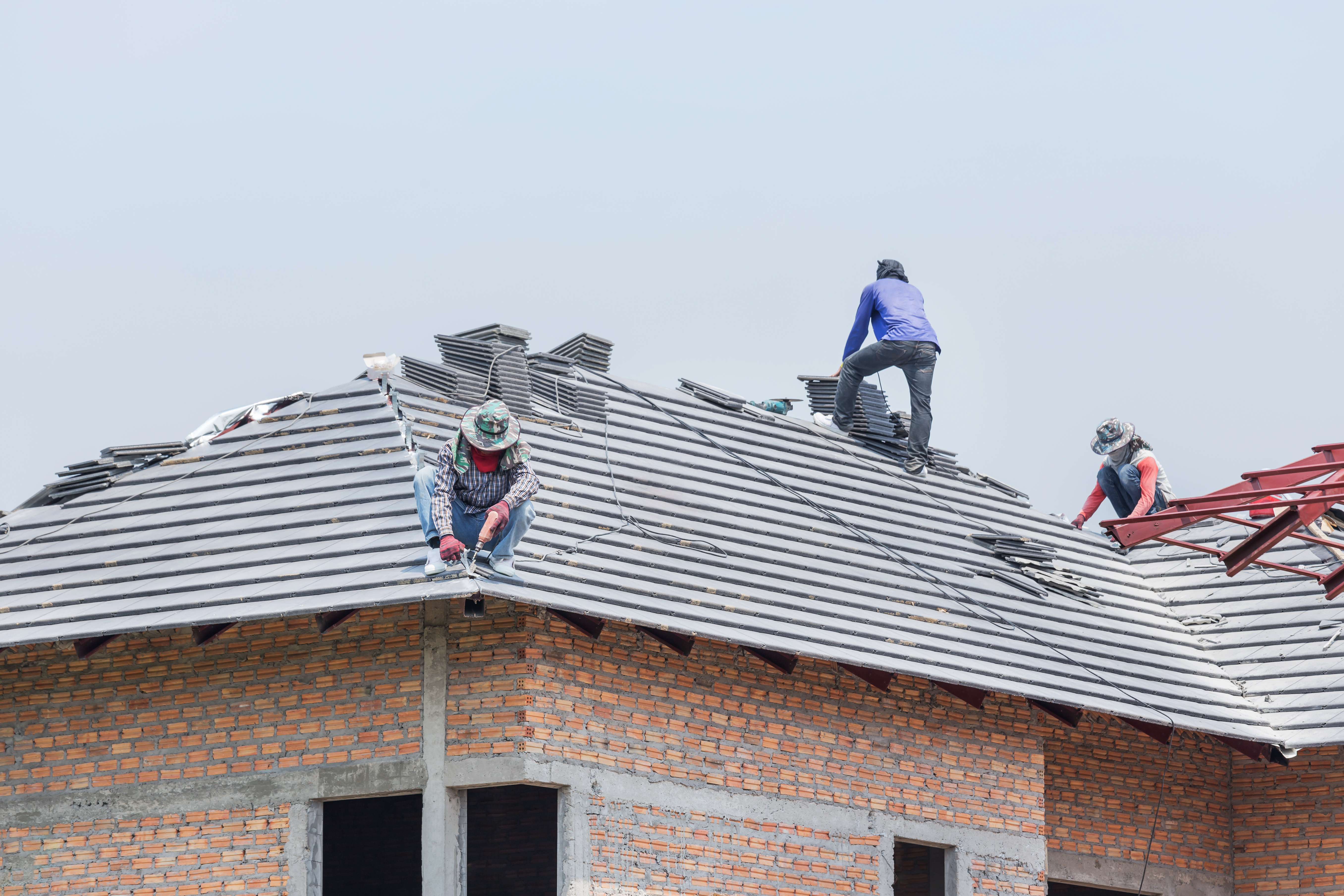 Workers installing concrete tiles on the roof while roofing house in construction site