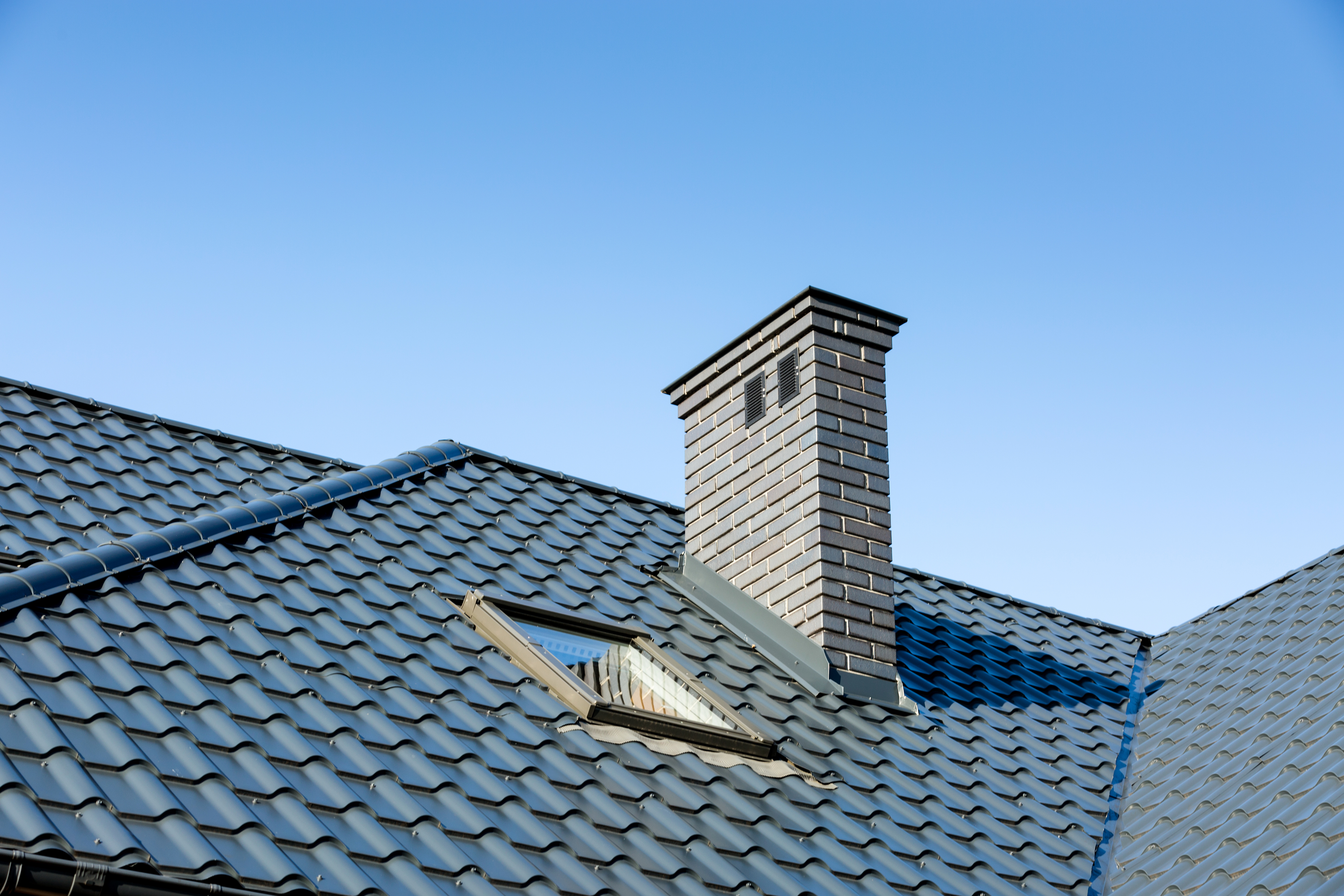 Roof of a detached house with a skylight and chimney against the sky